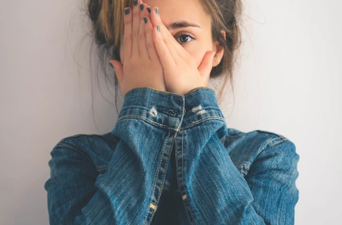 Teenage girl hiding side of her face with both hands wearing denim shirt